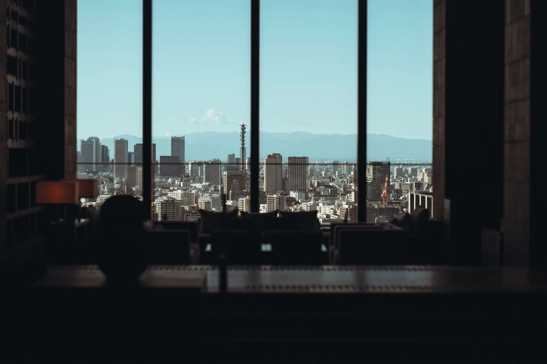 A city skyline seen through the tall windows of a dark office