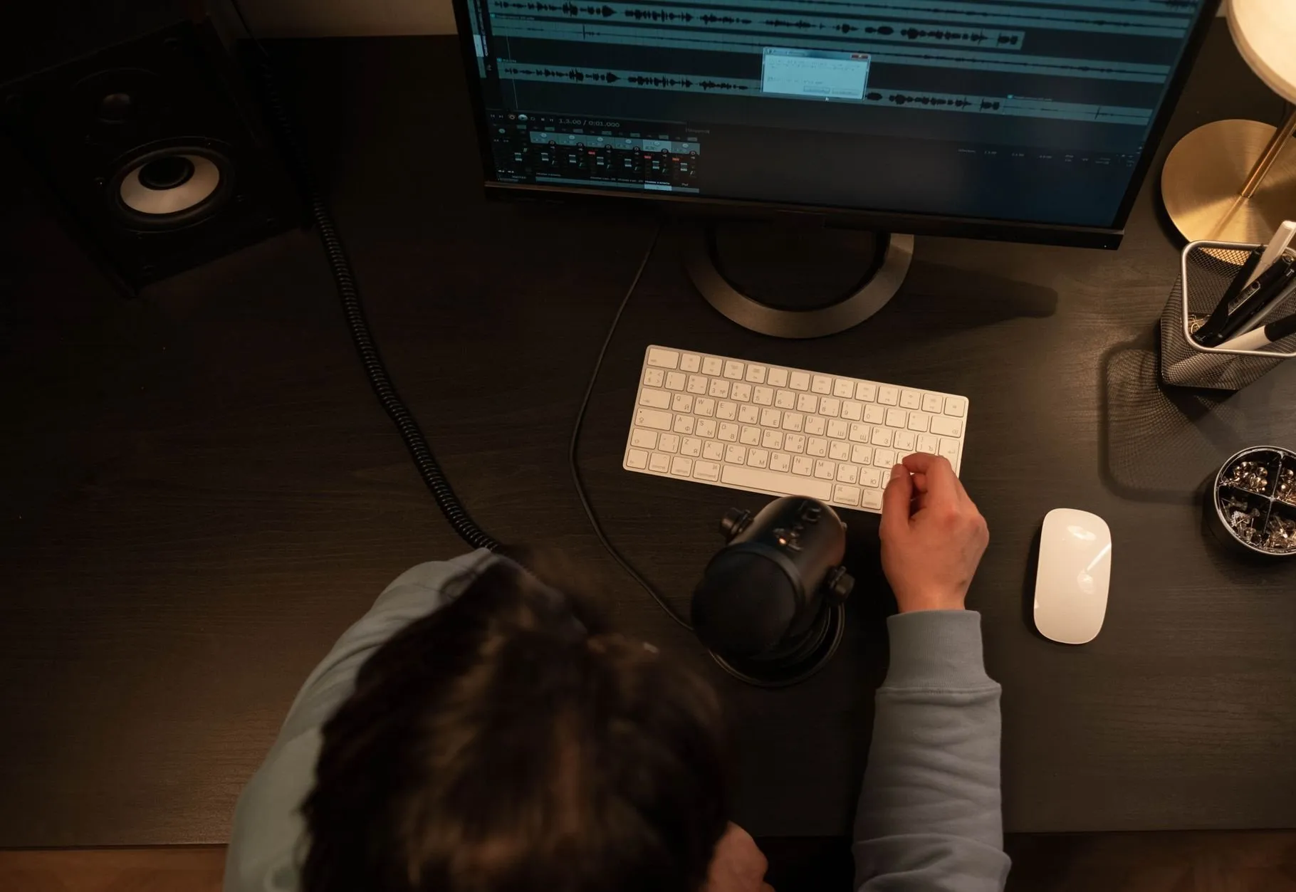 A person at a dark desk seen from above, one hand on a white keyboard