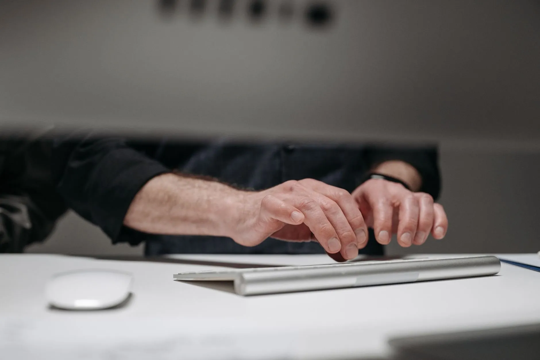 Hands resting above a slim white keyboard on a pale desk